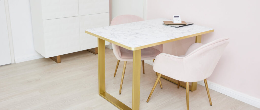 An einem Tisch mit goldenen Beinen stehen zwei pinke Samt-Sessel  - an diesem Tisch wird man zu den Beauty-Leistungen beraten.